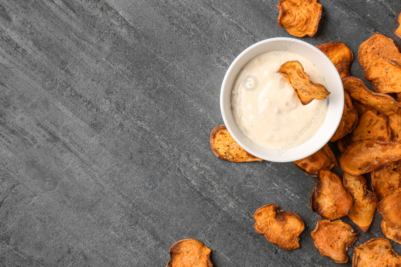 Photo of Sweet potato chips and bowl of sauce on grey background, top view. Space for text