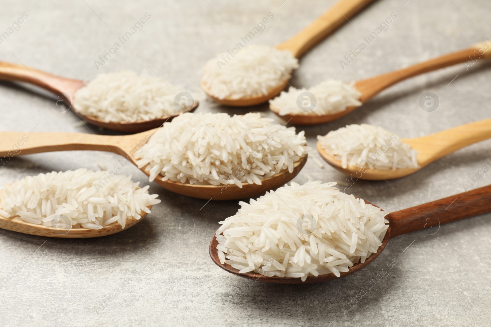 Photo of Raw basmati rice in spoons on grey table, closeup