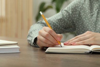 Woman writing in notebook at wooden table indoors, closeup