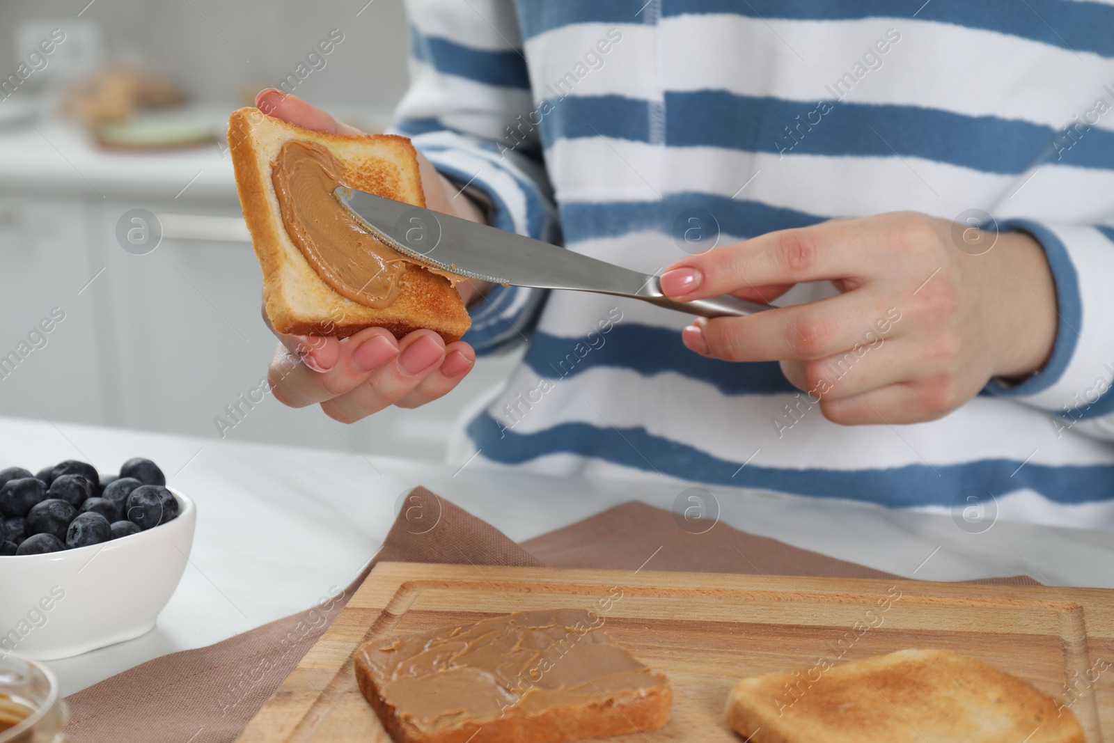 Photo of Woman spreading tasty nut butter onto toast at table, closeup