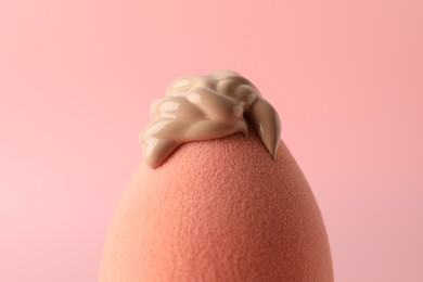 Photo of Makeup sponge with skin foundation on pink background, closeup