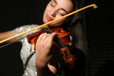 Photo of Beautiful young woman playing violin in dark room, focus on hand
