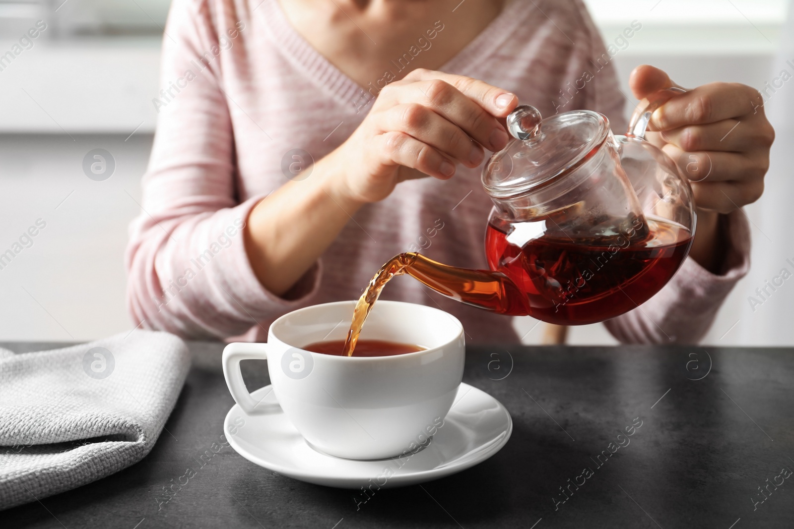 Photo of Woman pouring tea into porcelain cup at table, closeup