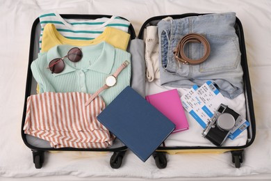 Photo of Open suitcase with clothes and accessories on bed, top view