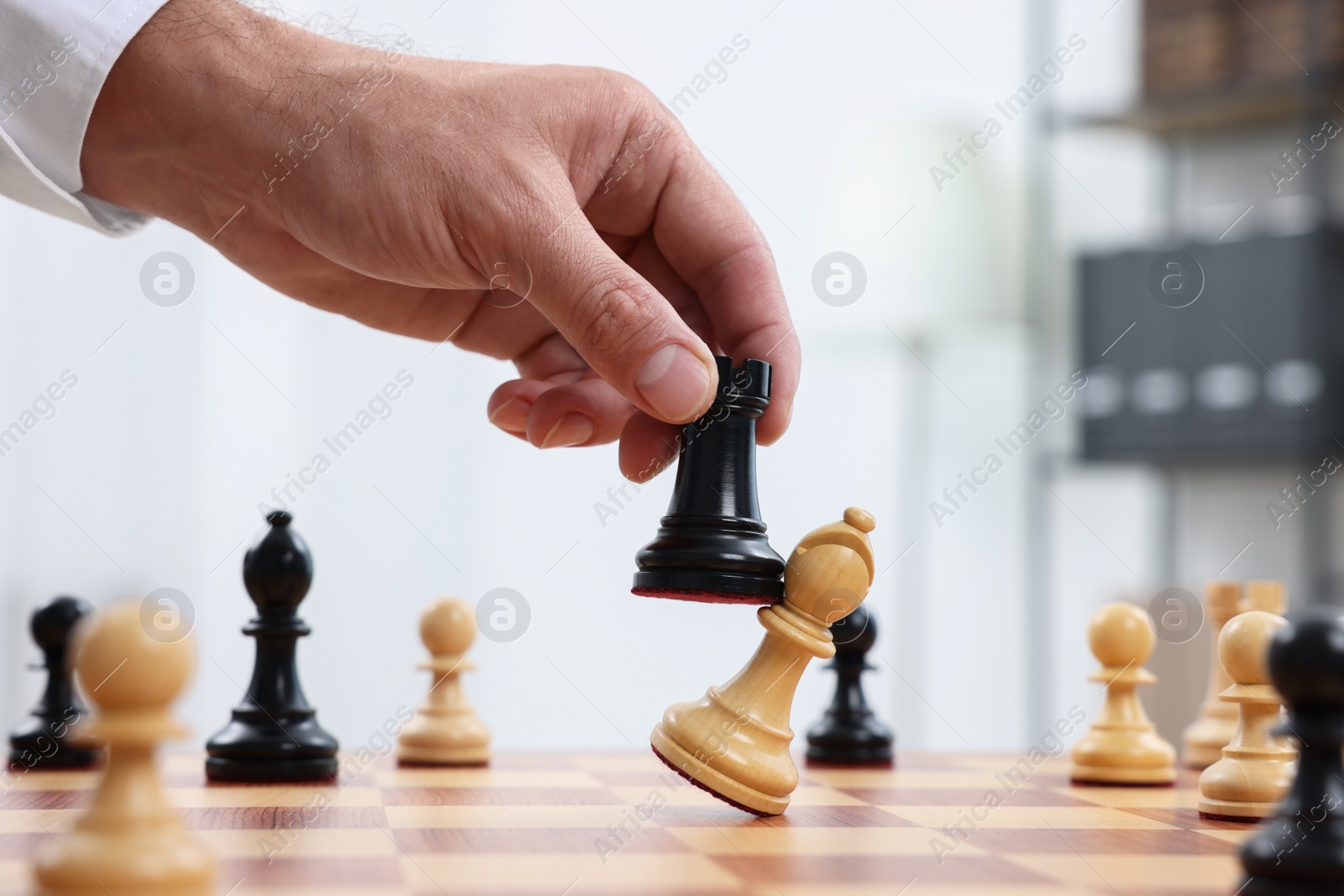 Photo of Man with rook game piece playing chess at checkerboard indoors, closeup