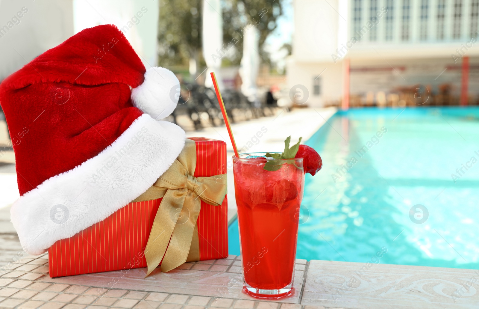 Photo of Authentic Santa Claus hat, gift box and cocktail near pool at resort