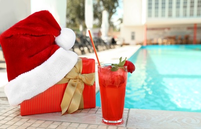 Photo of Authentic Santa Claus hat, gift box and cocktail near pool at resort