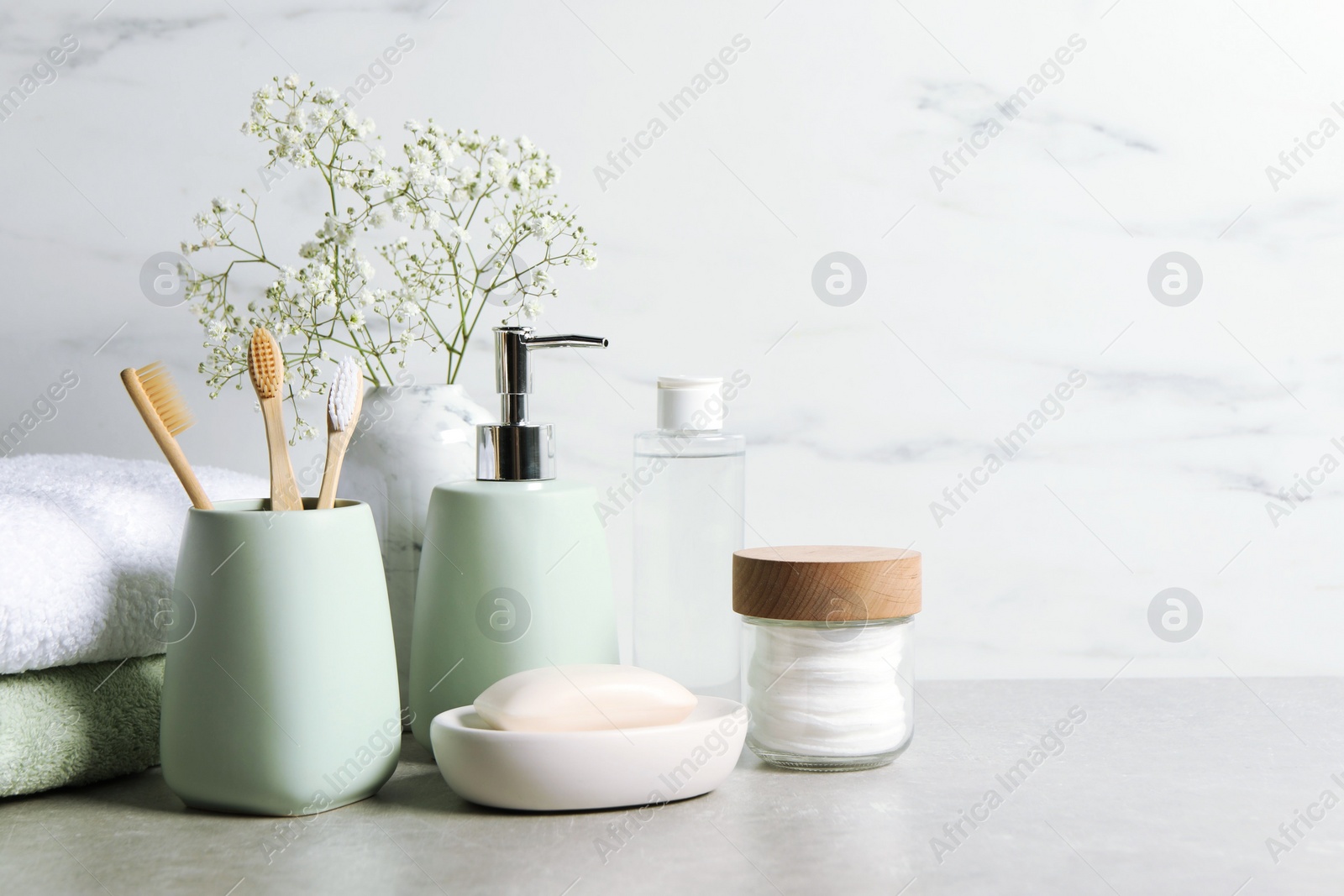Photo of Different bath accessories, personal care products and gypsophila flowers in vase on gray table near white marble wall, space for text