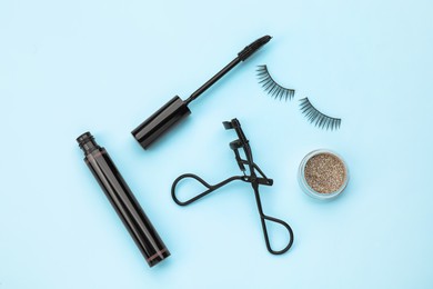 Eyelash curler and makeup products on light blue background, flat lay