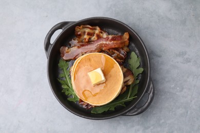 Photo of Tasty pancakes with butter, fried bacon and fresh arugula on grey table, top view