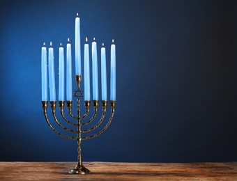 Photo of Hanukkah celebration. Menorah with burning candles on wooden table against blue background, space for text