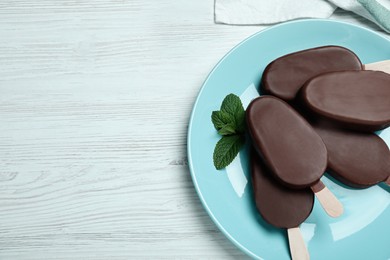 Glazed ice cream bars with fresh mint and chocolate on white wooden table, flat lay. Space for text