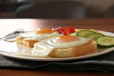 Tasty toasts with fried eggs, cheese and vegetables on wooden table, closeup