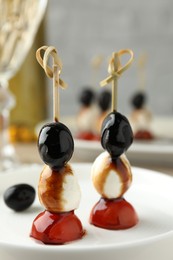 Tasty canapes with black olives, mozzarella and cherry tomatoes on table, closeup