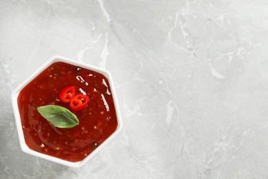 Spicy chili sauce with basil on light grey table, top view. Space for text