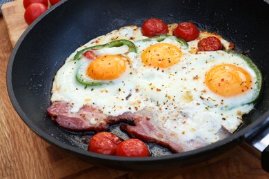 Delicious fried eggs with bacon, tomatoes and pepper served on wooden table, closeup