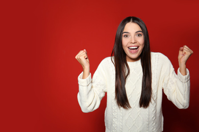 Excited woman wearing warm sweater on red background. Space for text