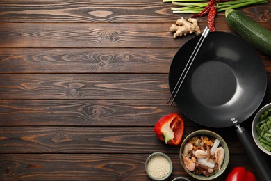 Black wok, chopsticks and products on wooden table, flat lay. Space for text