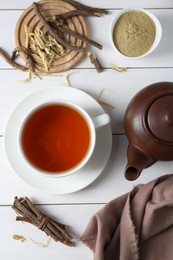 Photo of Aromatic licorice tea in cup, dried sticks of licorice root and powder on white wooden table, flat lay