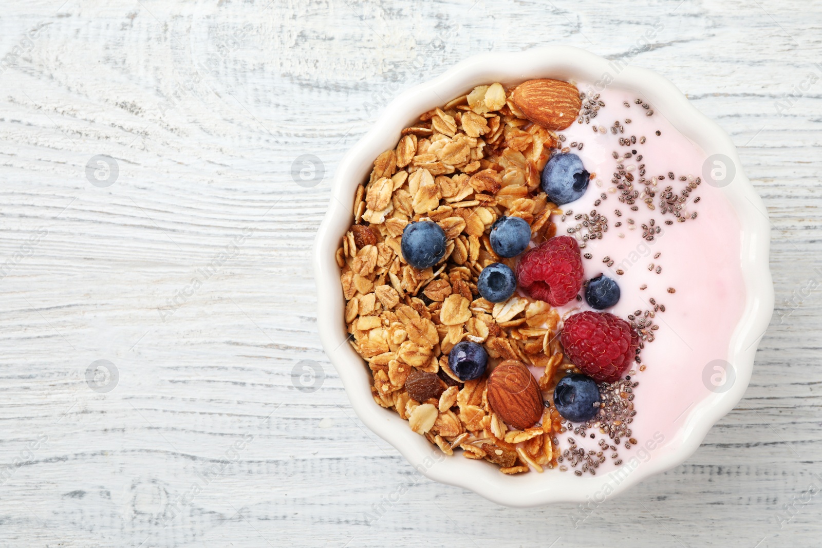 Photo of Tasty homemade granola served on white wooden table, top view with space for text. Healthy breakfast