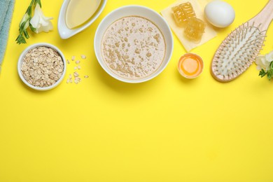 Photo of Homemade hair mask in bowl, ingredients and wooden brush on yellow background, flat lay. Space for text