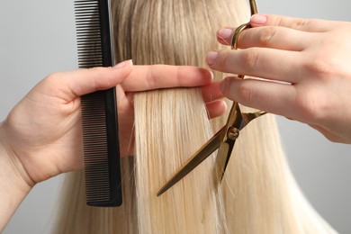 Photo of Hairdresser cutting client's hair with scissors on light grey background, closeup