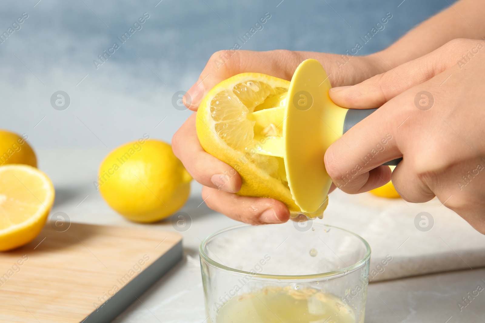 Photo of Woman squeezing lemon juice with reamer into glass on table