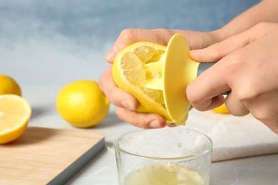 Woman squeezing lemon juice with reamer into glass on table