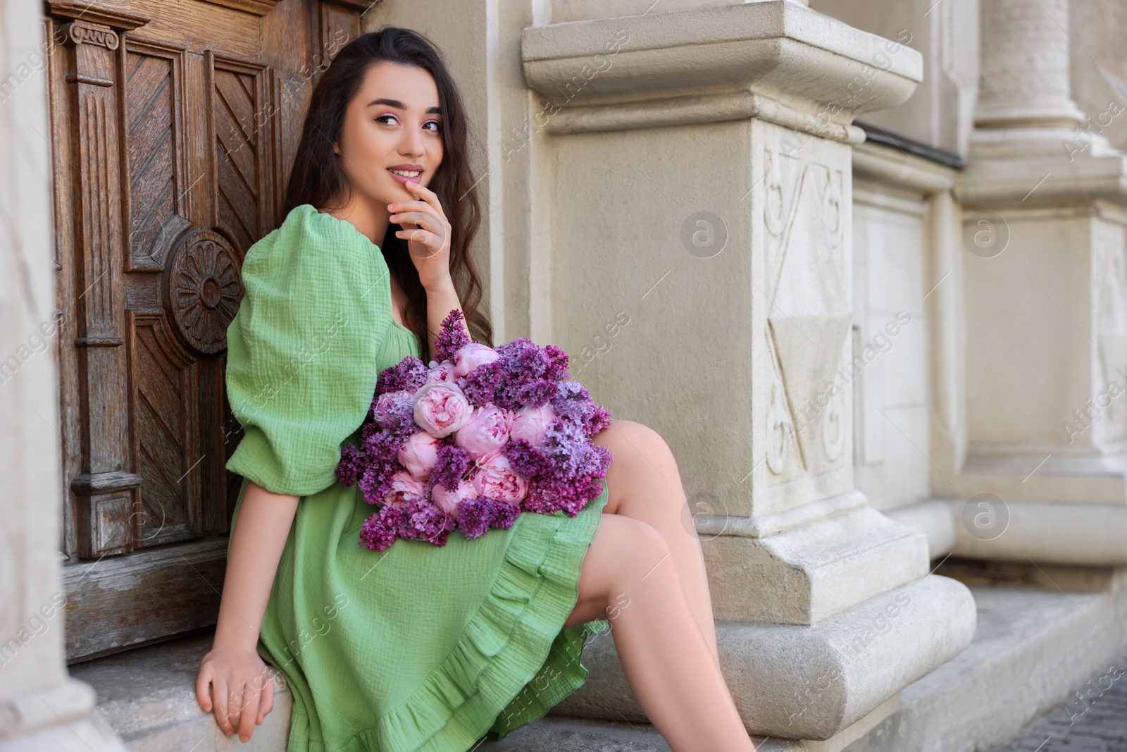 Photo of Beautiful woman with bouquet of spring flowers near building outdoors, space for text