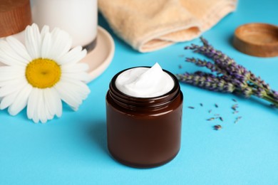 Photo of Jar of face cream and beautiful flowers on light blue table