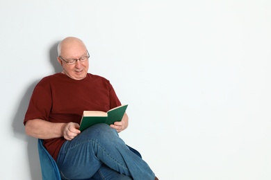 Portrait of senior man with glasses reading book on light background. Space for text