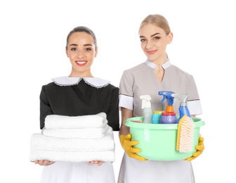 Young chambermaids with folded clean towels and detergents on white background