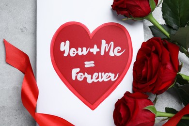 Photo of Card with love message near red roses on grey table, flat lay