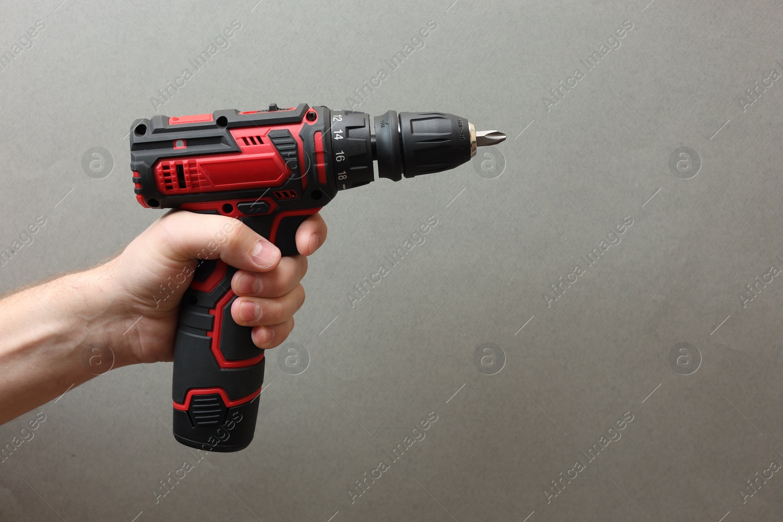 Photo of Handyman holding electric screwdriver on grey background, closeup. Space for text