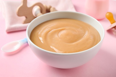 Bowl of healthy baby food on pink background, closeup