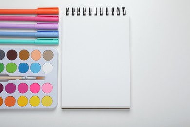Photo of Watercolor palette, empty notebook and colorful markers on white background, flat lay. Space for text