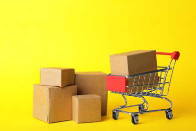 Photo of Shopping cart and boxes on yellow background. Logistics and wholesale concept