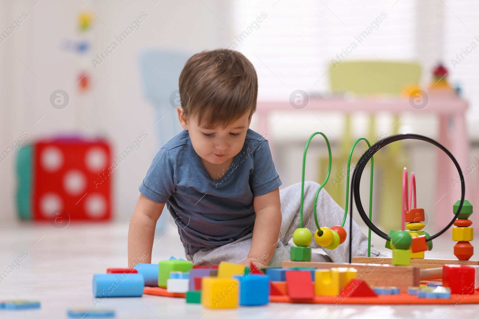 Photo of Cute little child playing with bead maze on floor at home