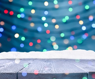 Image of Wooden surface with heap of snow and blurred Christmas lights on background, bokeh effect 