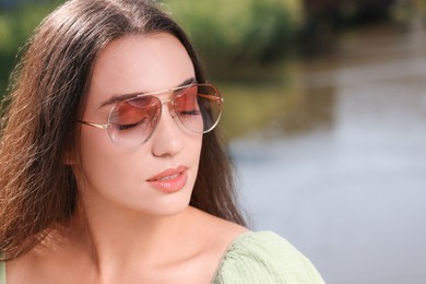 Beautiful woman in sunglasses near river, space for text