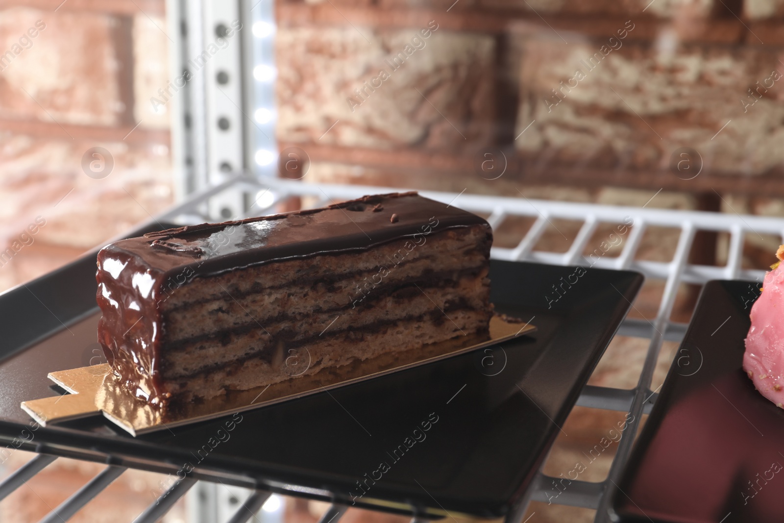 Photo of Display case with piece of delicious chocolate cake on shelf in cafe, closeup