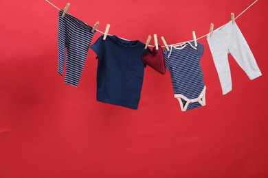 Photo of Different baby clothes and heart shaped cushion drying on laundry line against red background