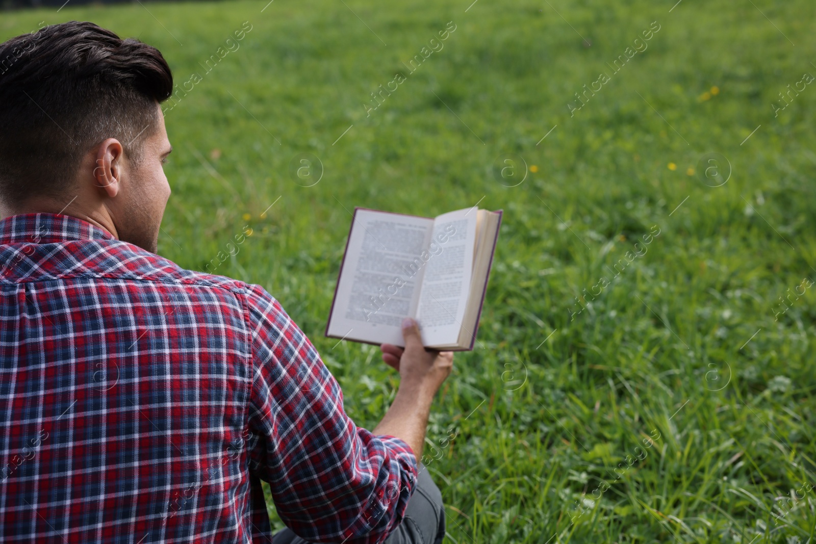 Photo of Man reading book on green grass, back view