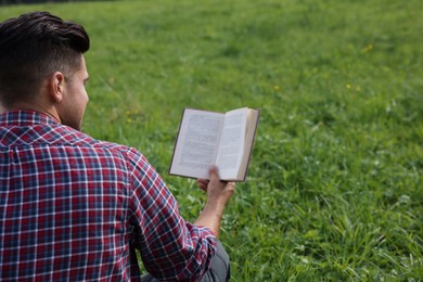 Photo of Man reading book on green grass, back view