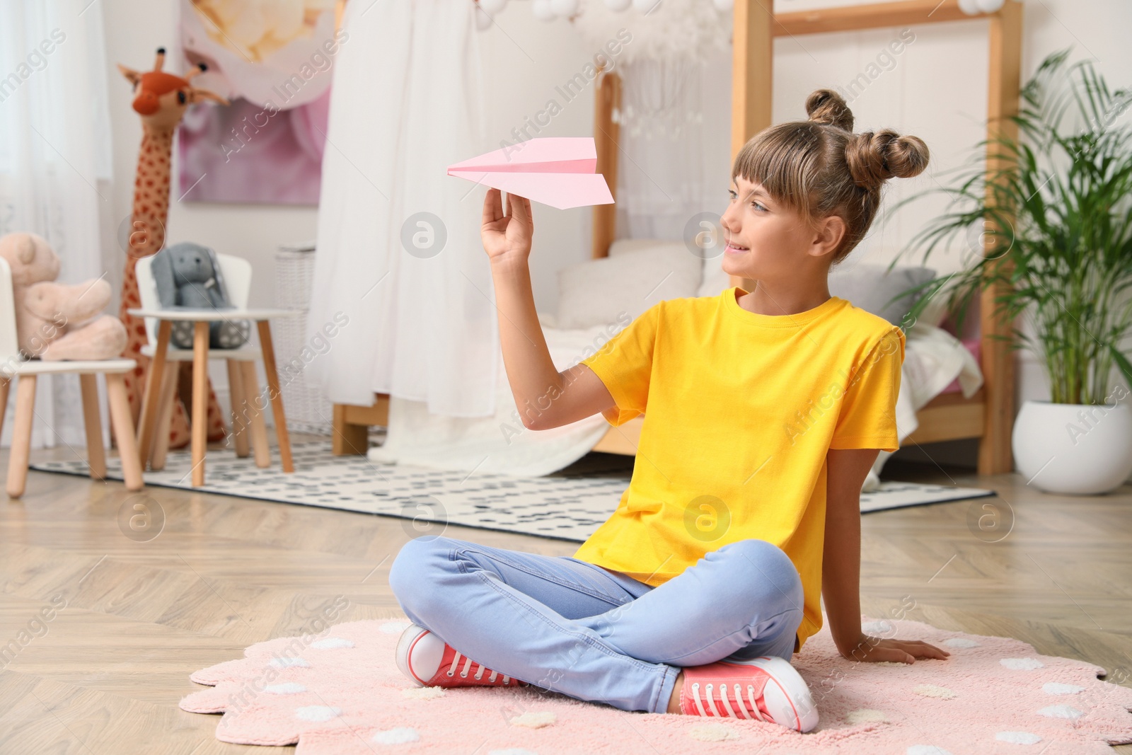 Photo of Cute little girl playing with paper plane on floor in room. Space for text