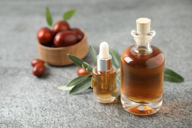 Photo of Glass bottles with jojoba oil on grey stone table. Space for text