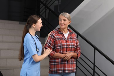 Photo of Young healthcare worker assisting senior woman on stairs indoors