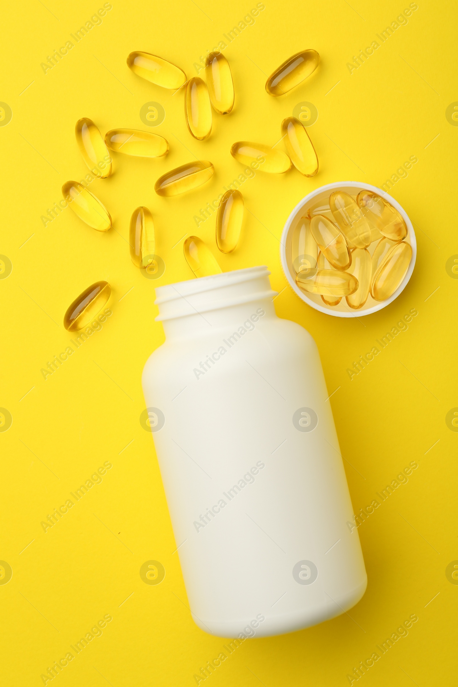 Photo of Softgel capsules, lid and bottle on yellow background, flat lay