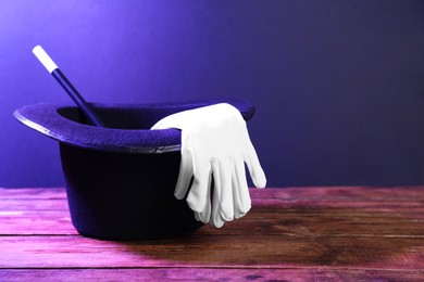Photo of Top hat, gloves and wand on wooden table, space for text. Magician equipment