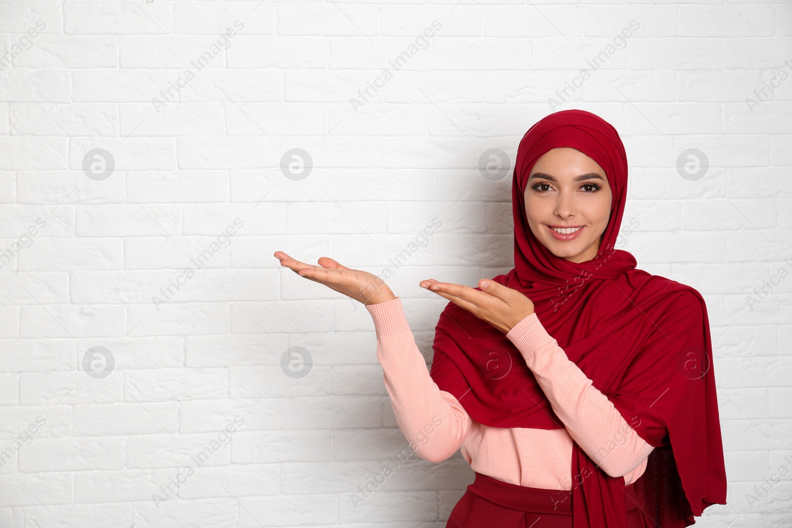 Photo of Portrait of young Muslim woman in hijab against brick wall. Space for text